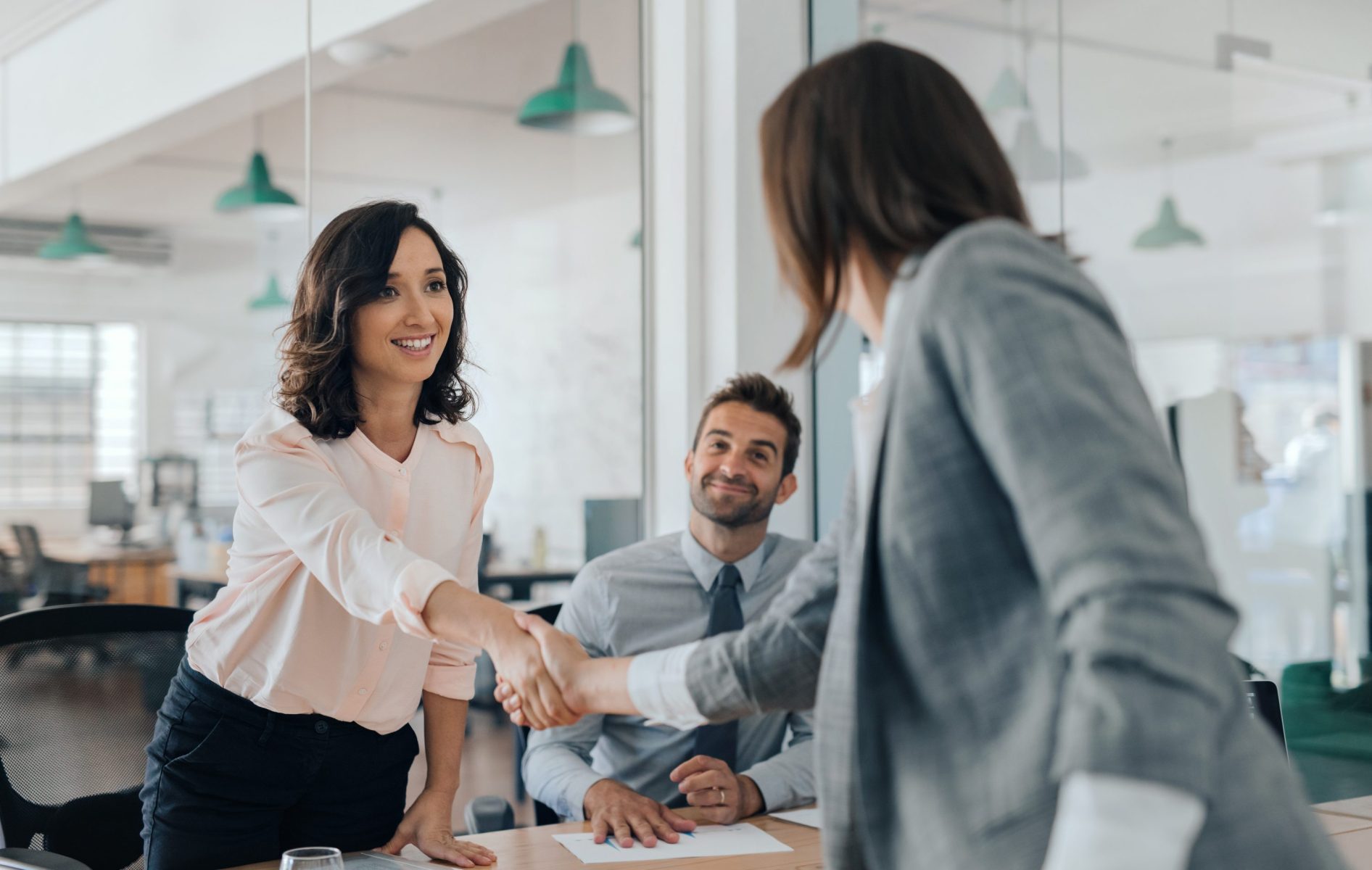 Smiling young businesswoman shaking hands with a coworker during a meeting with colleagues around a table in an office boardroom