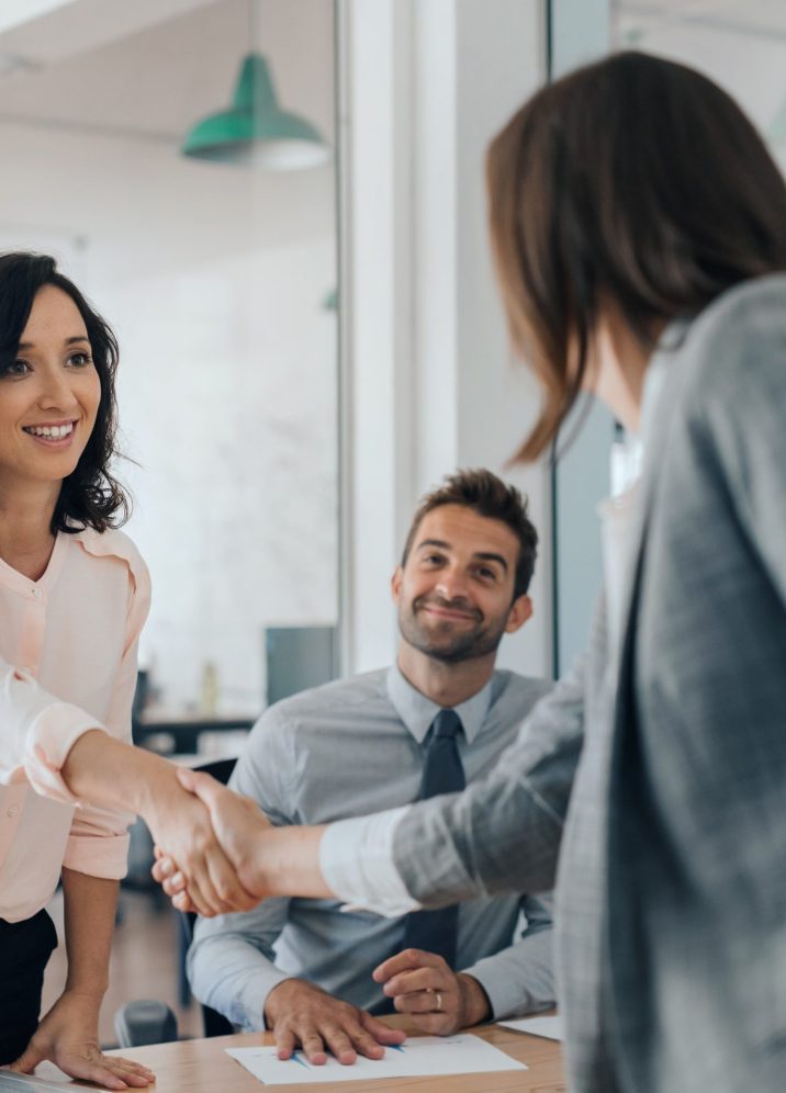 Smiling young businesswoman shaking hands with a coworker during a meeting with colleagues around a table in an office boardroom
