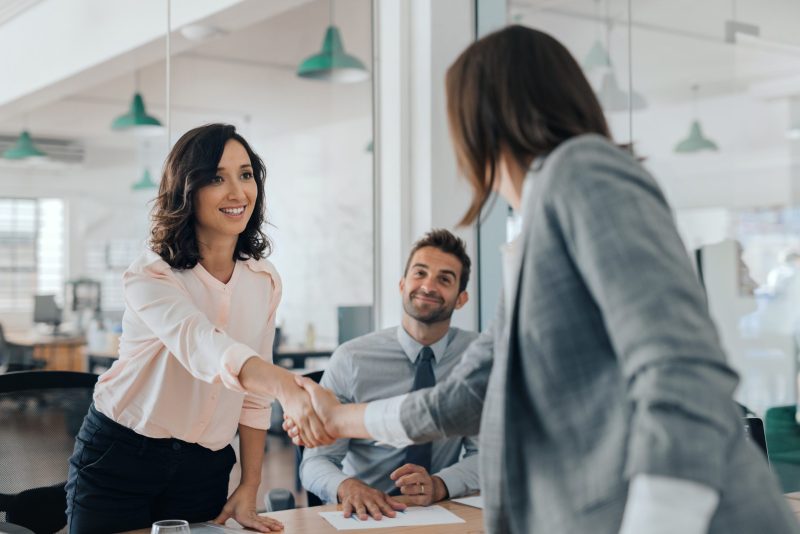 Smiling young businesswoman shaking hands with a coworker during a meeting with colleagues around a table in an office boardroom