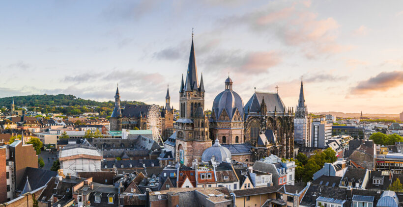 Panoramaaufnahme der Stadt Aachen mit dem Aachener Dom und Rathaus im Sonnenuntergang.