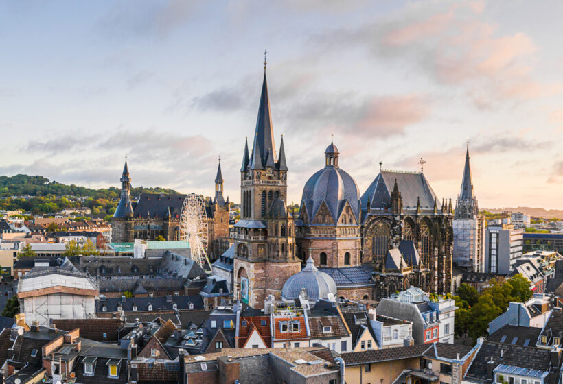 Panoramaaufnahme der Stadt Aachen mit dem Aachener Dom und Rathaus im Sonnenuntergang.
