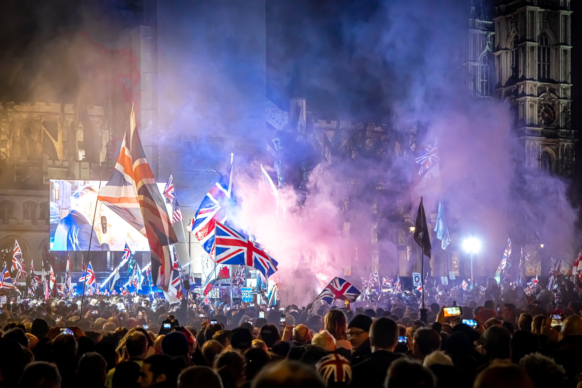 Menschenmenge mit britischen Flaggen feiert in einer nächtlichen Szene mit Rauch und Scheinwerfern.