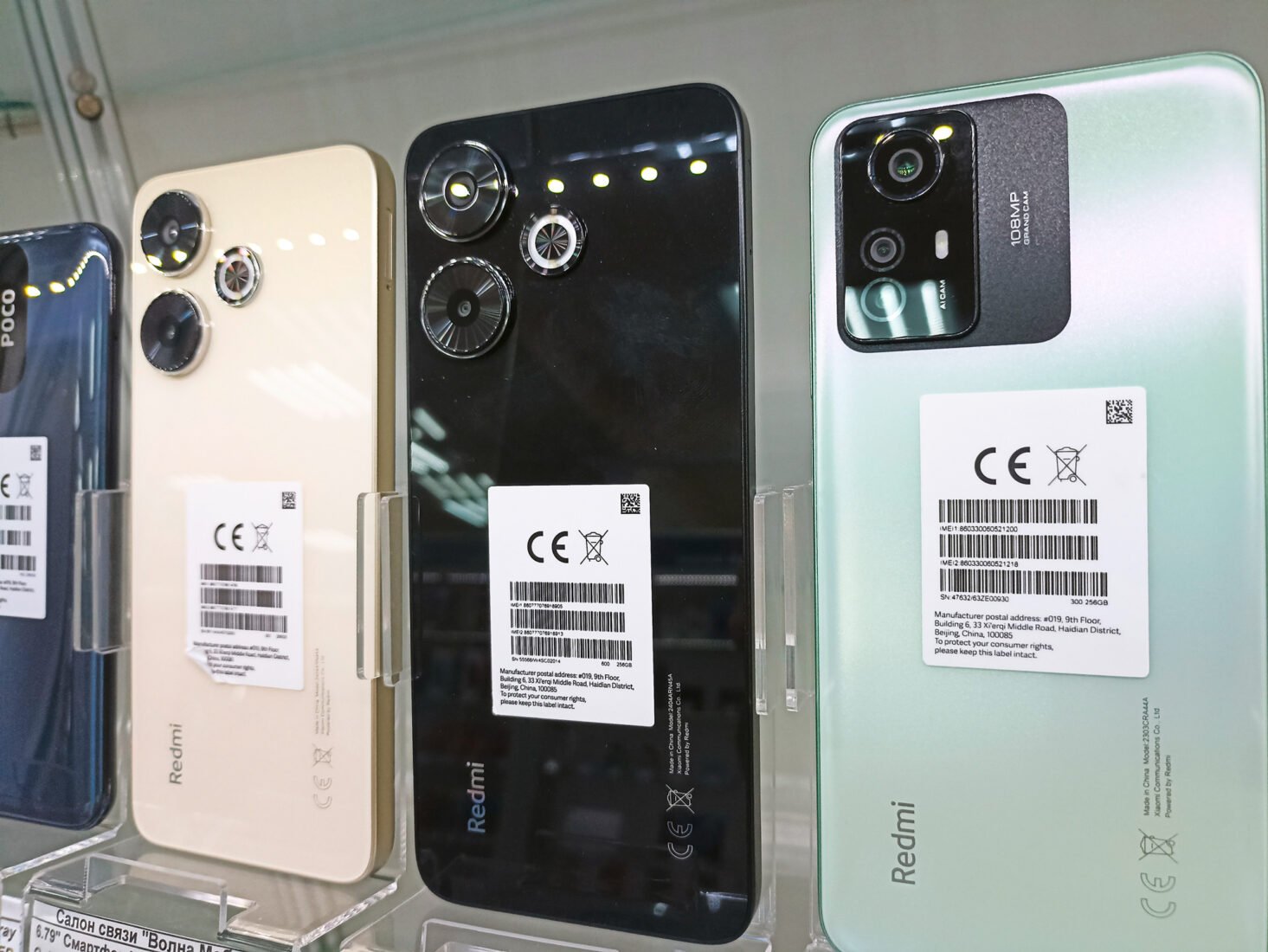 Verschiedene Smartphones mit CE-Kennzeichnung und Produkthinweisen auf der Rückseite in einer Verkaufsvitrine.