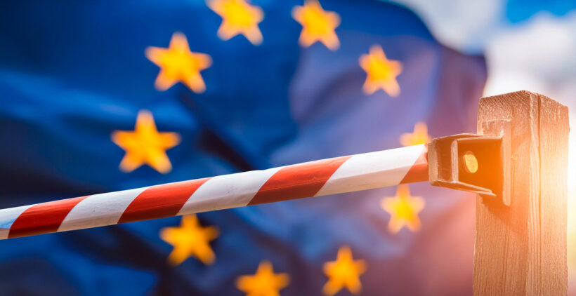 Schranke mit rot-weißen Streifen vor wehender Europaflagge im Hintergrund.