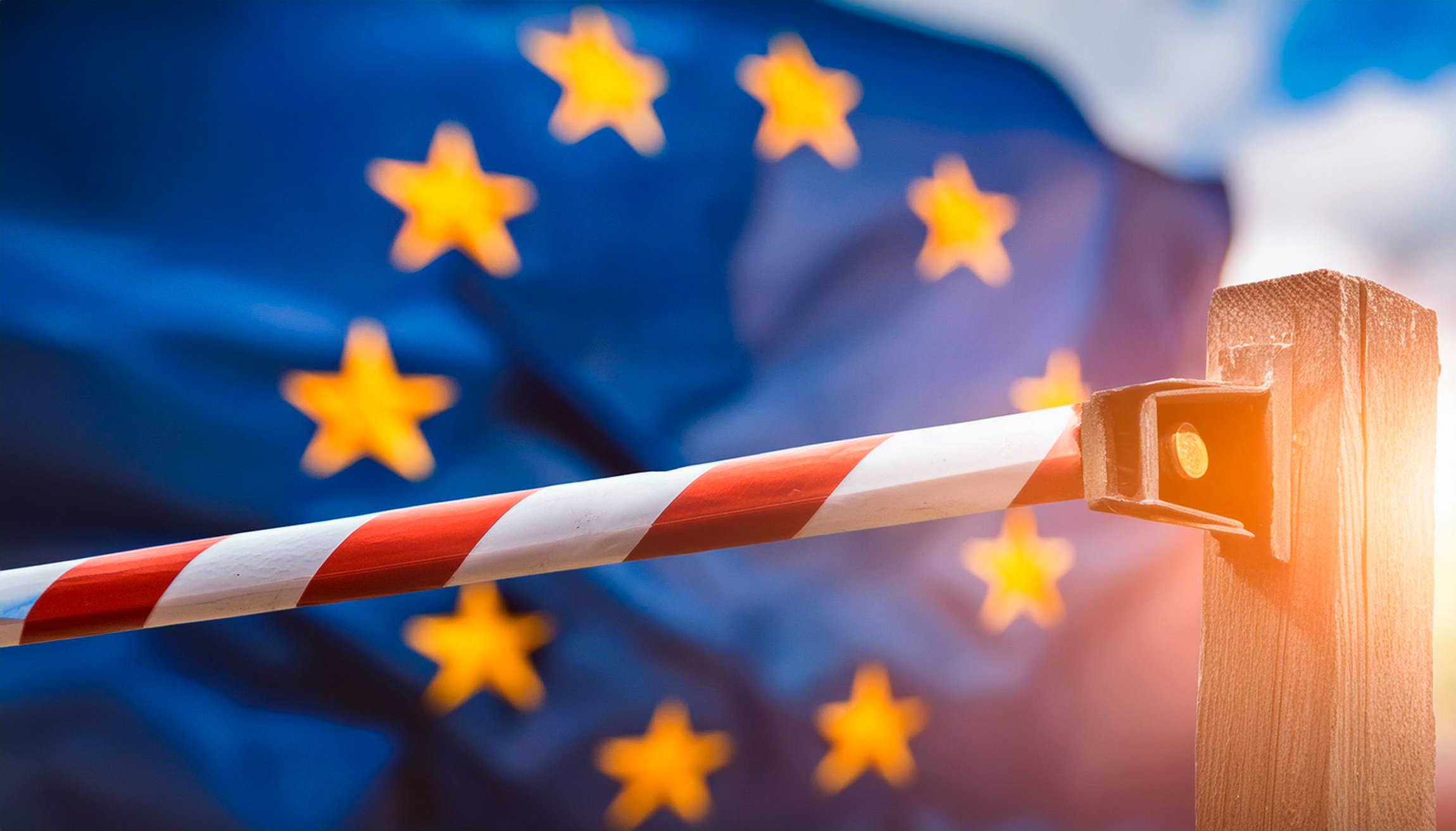 Schranke mit rot-weißen Streifen vor wehender Europaflagge im Hintergrund.