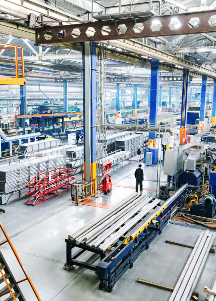 Weitläufige Industriehalle mit Maschinen, Metallteilen und einem Arbeiter, der durch die Fertigungshalle geht.