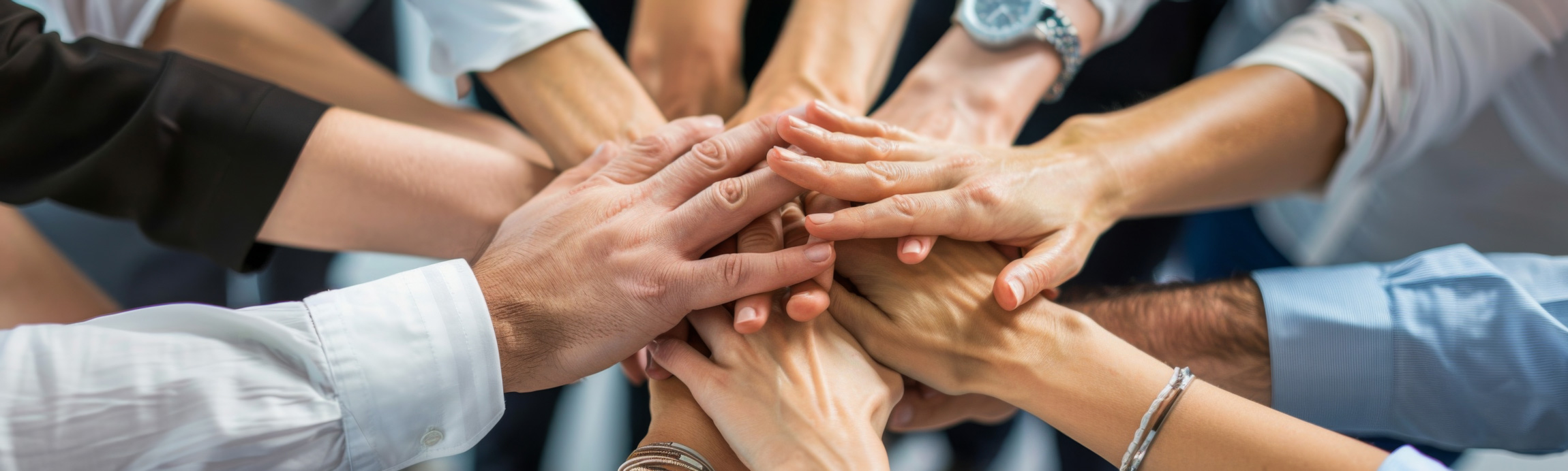 Mehrere Hände unterschiedlicher Personen, die sich in der Mitte übereinanderlegen – ein starkes Symbol für Teamwork, Zusammenhalt und gemeinsames Engagement.