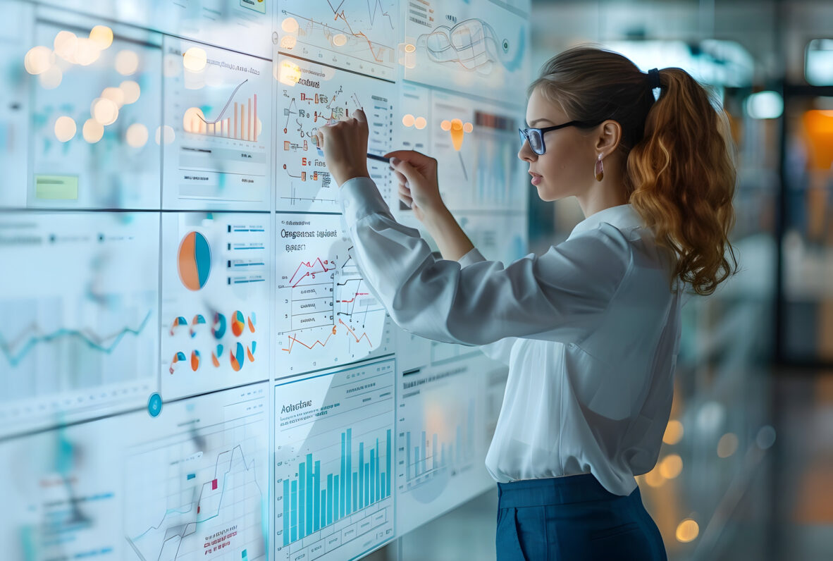 Junge Frau analysiert interaktive Diagramme auf einem großen digitalen Bildschirm in einem modernen Büro.