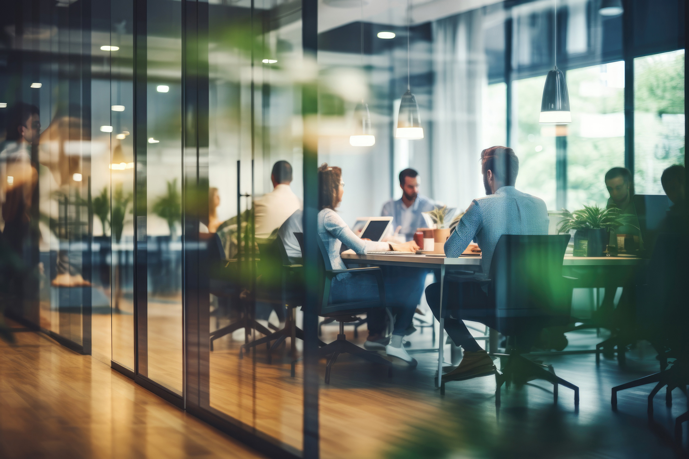 Ein Team sitzt in einem modernen Büro mit Glaswänden und bespricht gemeinsam Projekte. Die Teilnehmer arbeiten mit Laptops und Dokumenten in einer hellen und einladenden Umgebung.
