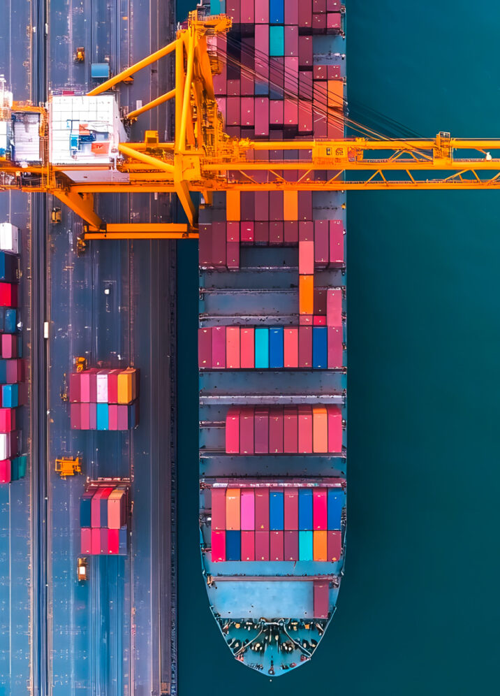 Luftaufnahme eines Containerhafens mit Frachtschiffen und bunten Containern, die von einem gelben Kran verladen werden.