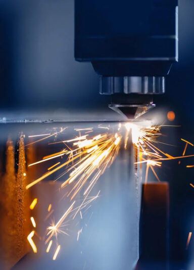 Nahaufnahme eines Laser-Schneidkopfs, der ein Metallstück bearbeitet. Funken sprühen während des Schneidprozesses, was die präzise industrielle Fertigungstechnologie verdeutlicht.