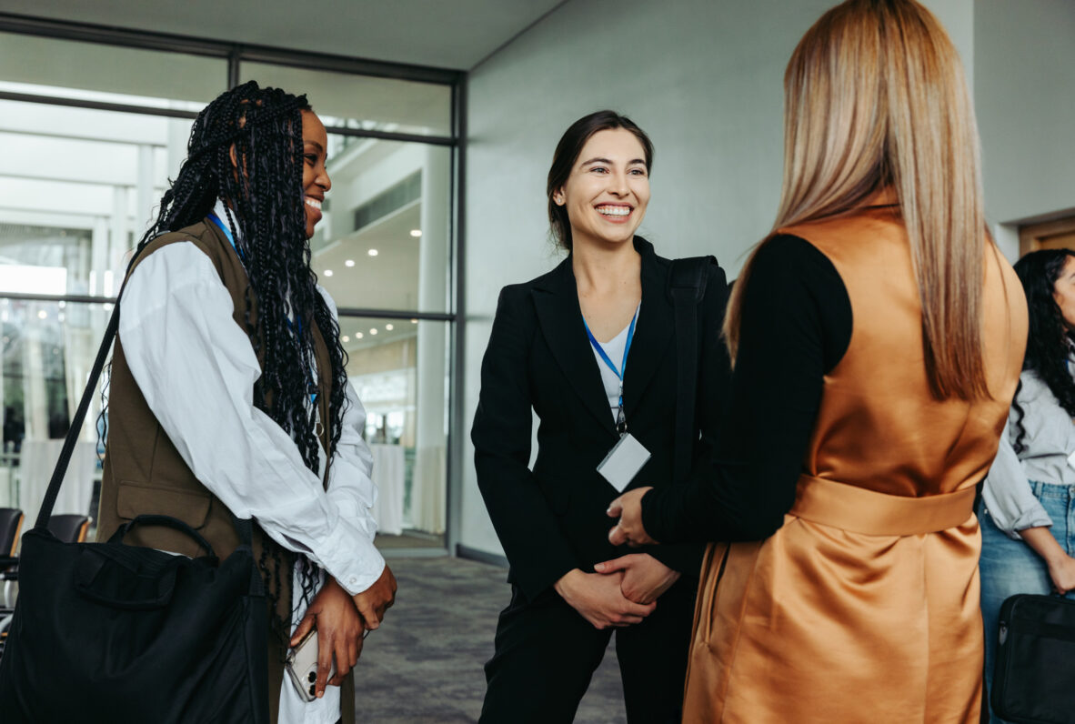 Drei Frauen im Gespräch bei einer Konferenz oder Netzwerkveranstaltung.
