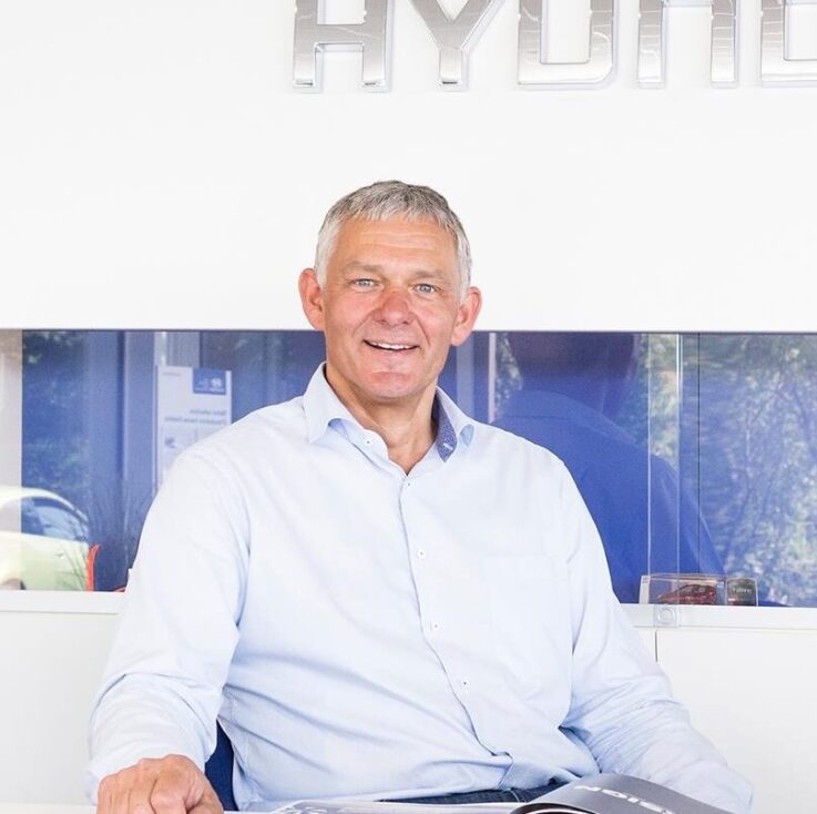 Michael Johnen, Geschäftsführer von Johnen Automobile, sitzt lächelnd an einem Tisch im Autohaus.